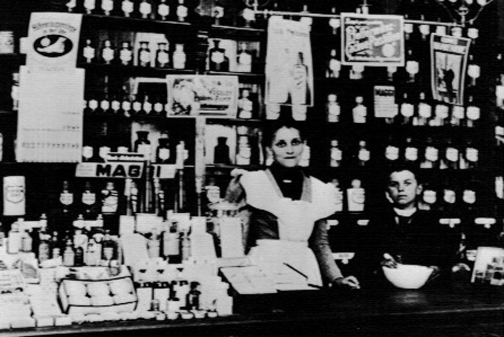 Bild der alten Theke mit Frau und Junge zu sehen. Um 1905 herum.